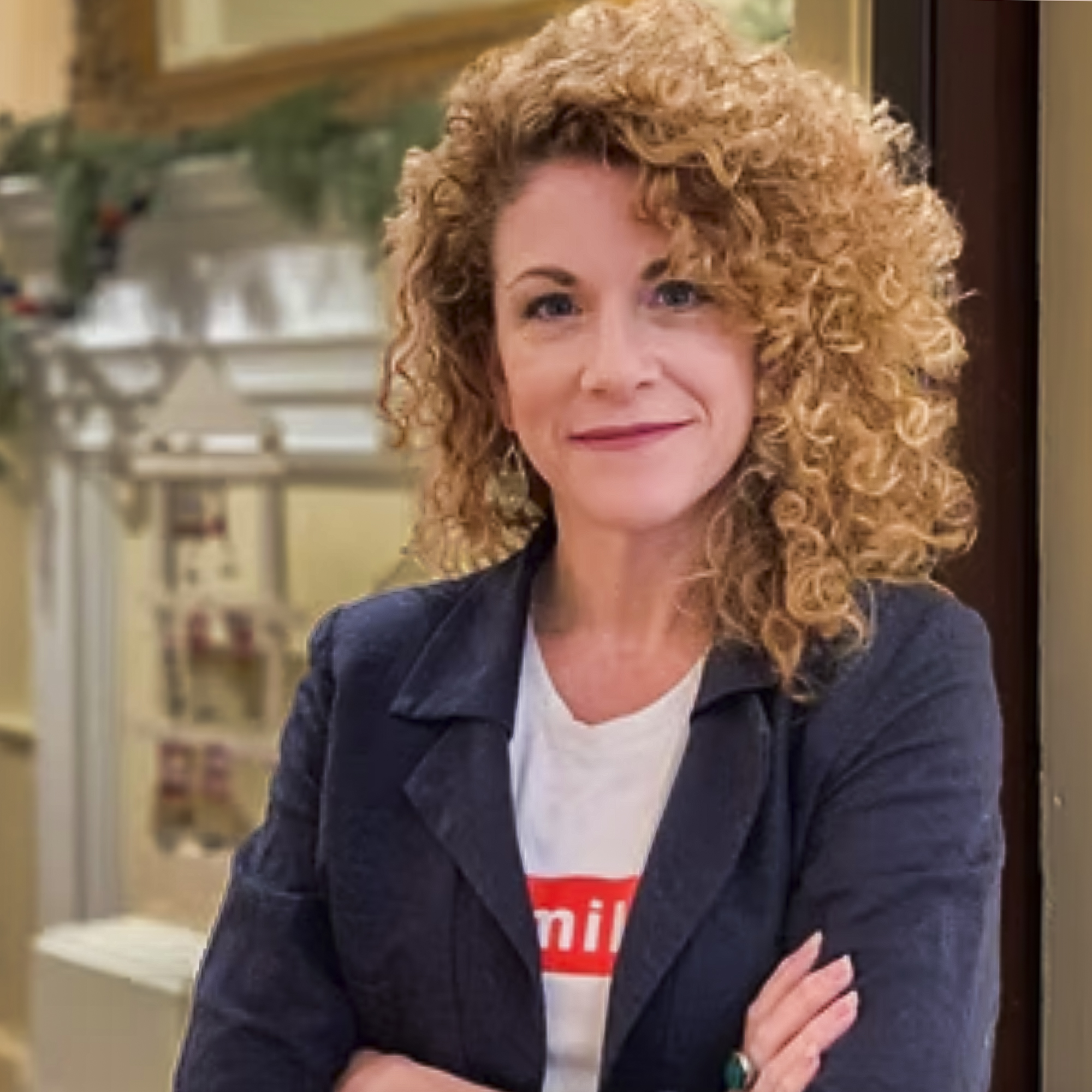 Woman with blonde curly hair and a blue blazer standing in a doorway