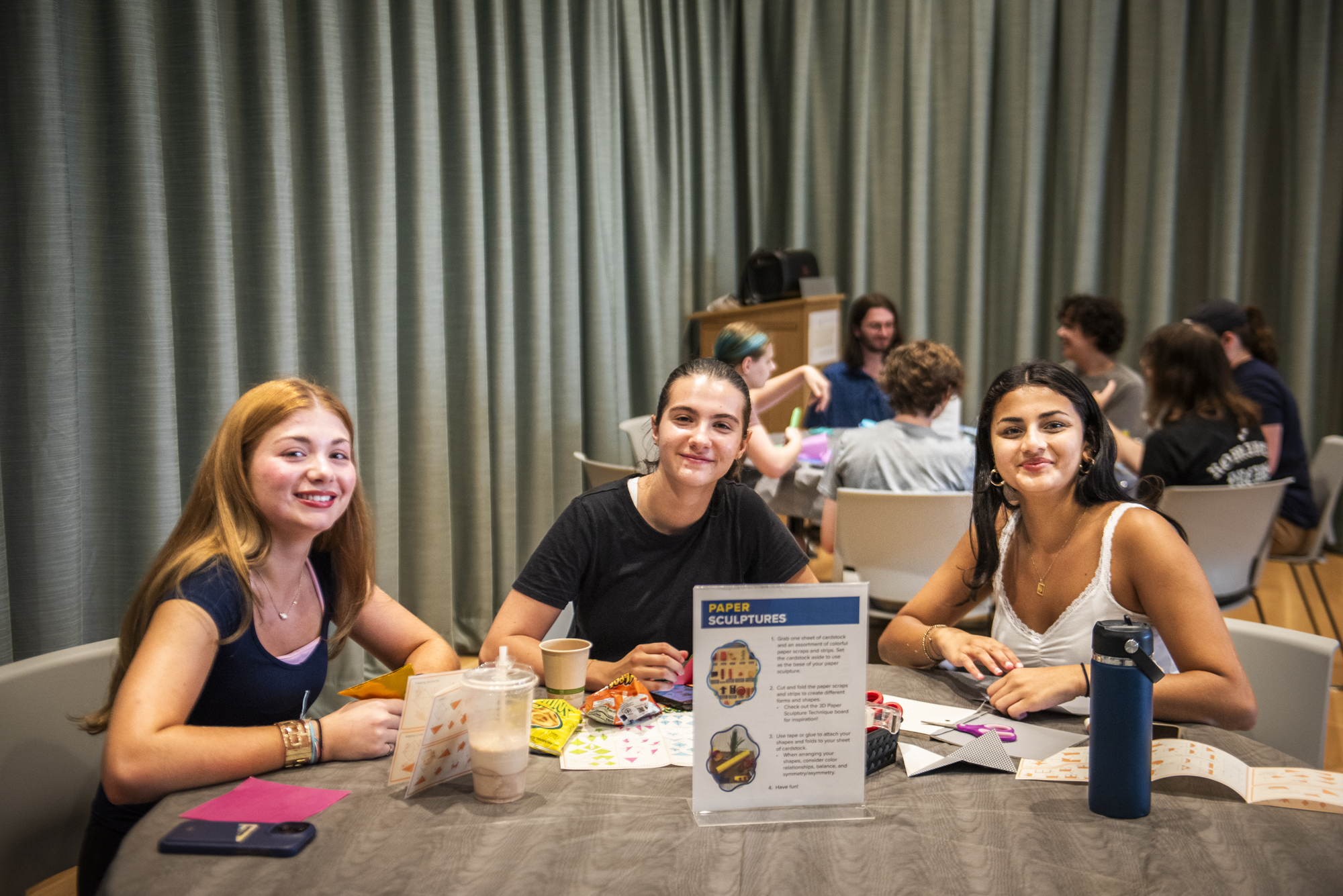 Three women sit at a table and make crafts