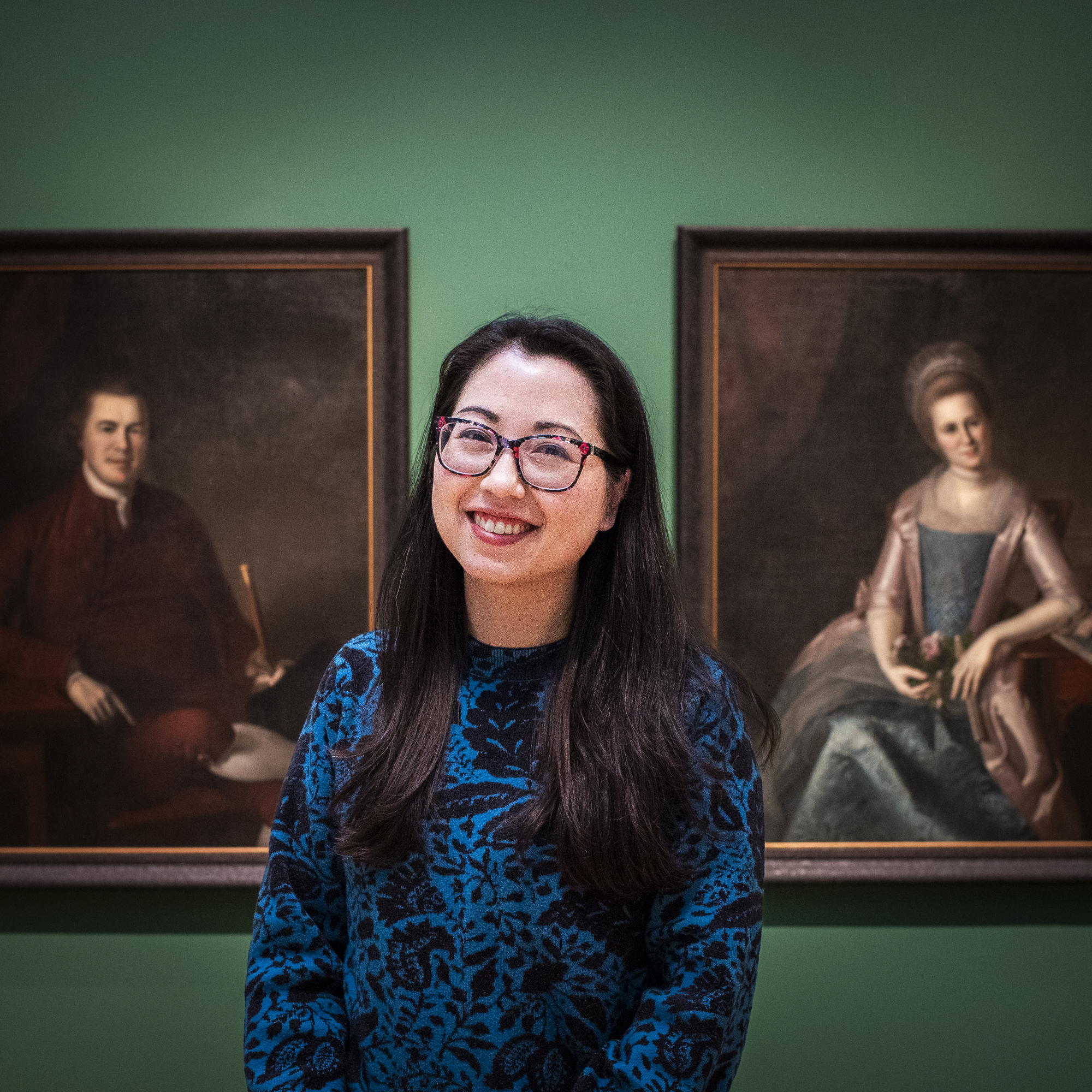 Woman with glasses standing in front of a green gallery wall