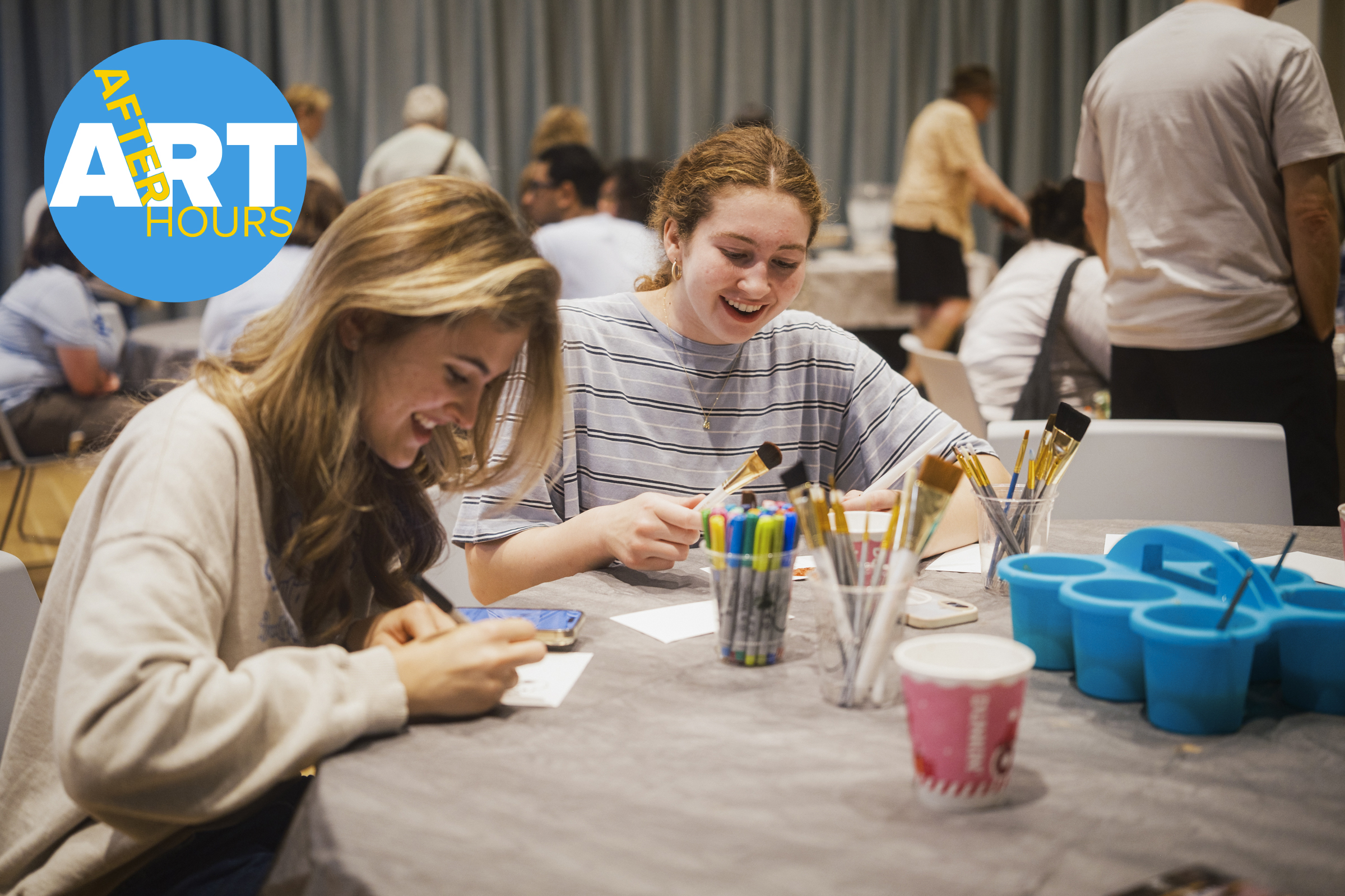 Young people sit at a table smiling and doing crafts. A blue logo with yellow and white "Art After Hours" text is located at top left.