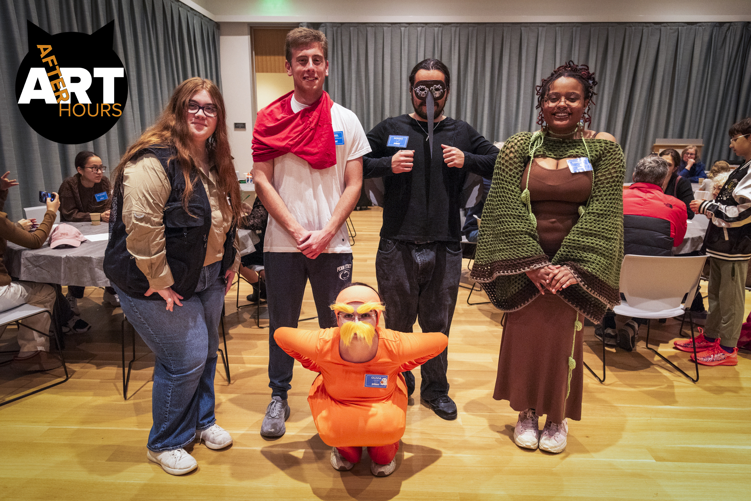 Image of a group of people in Halloween costumes at an event in a curtained room. Image has a black cat "Art After Hours" logo in the top left corner.