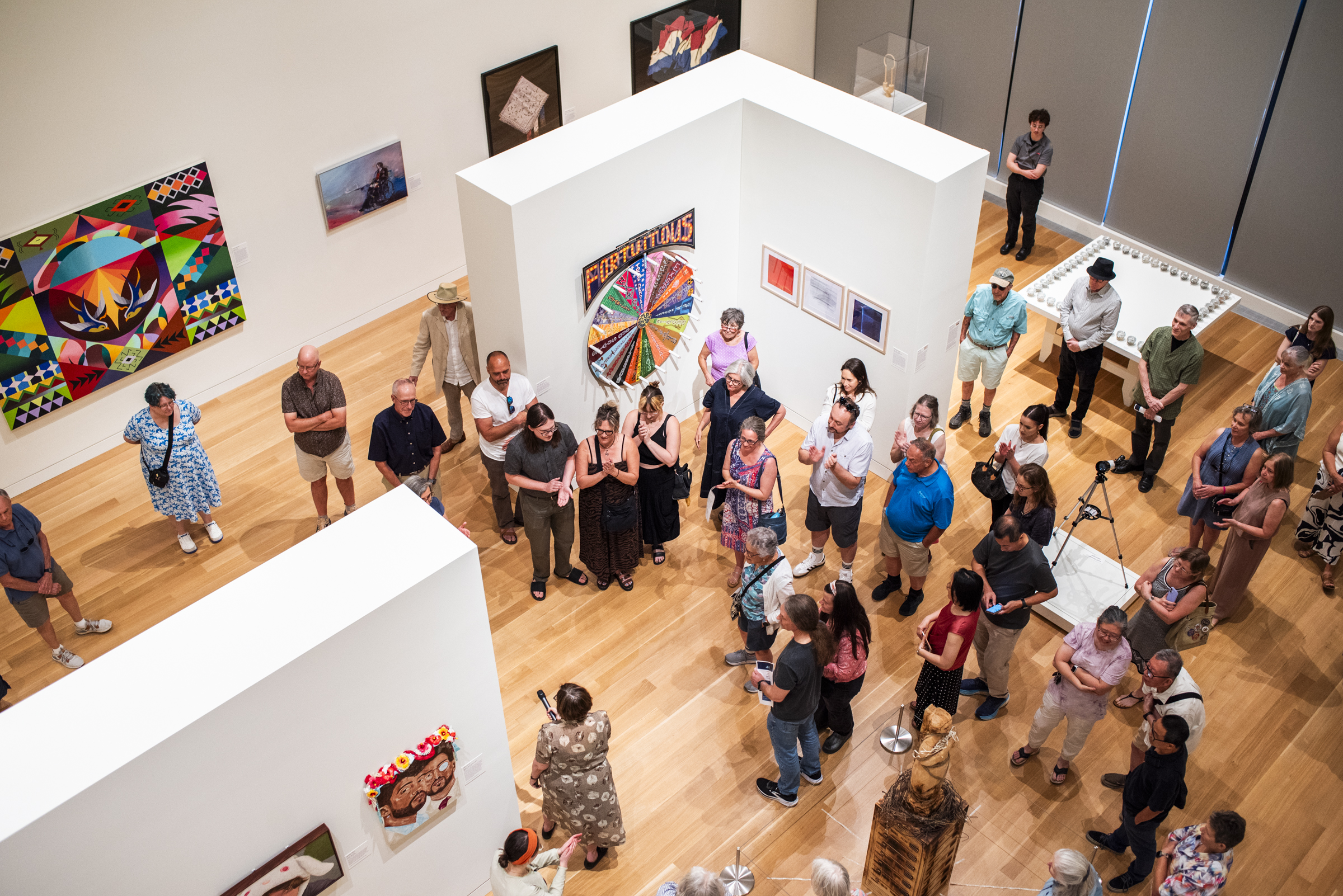 Overhead view of a large group of people in an art gallery listening to an artist talk about their artwork.
