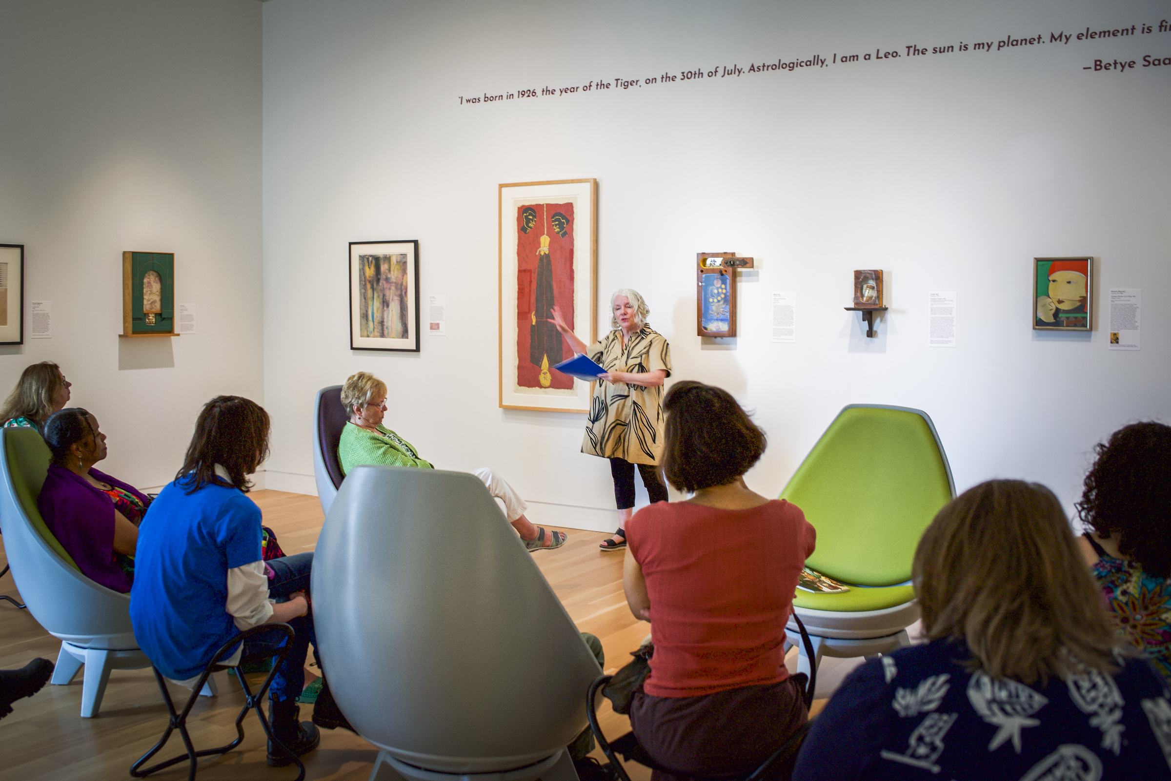 People on chairs in an art gallery listening to a speaker.