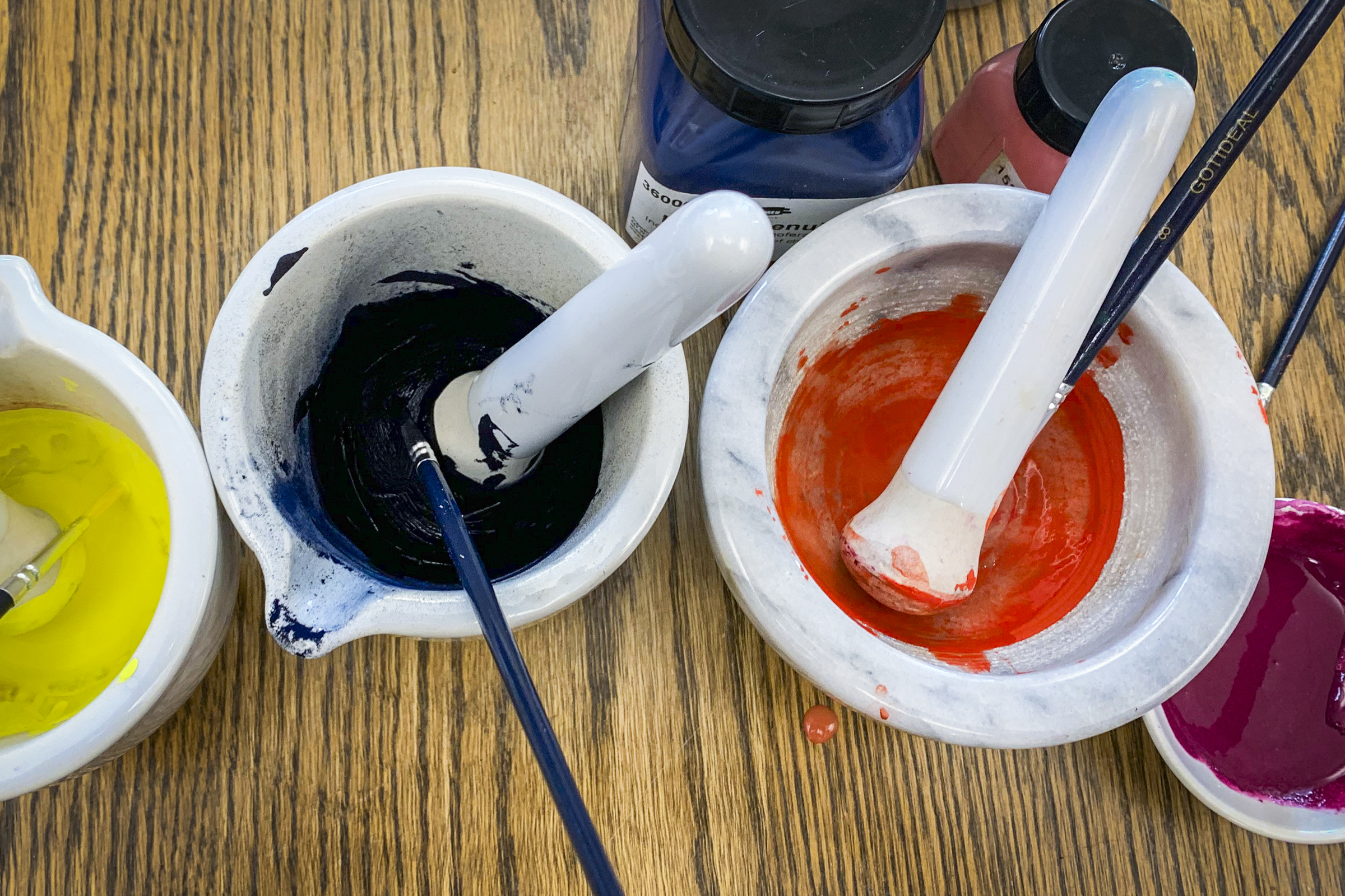 Overhead view of paint in yellow, blue, orange, and red in white mortar and pestle jars.